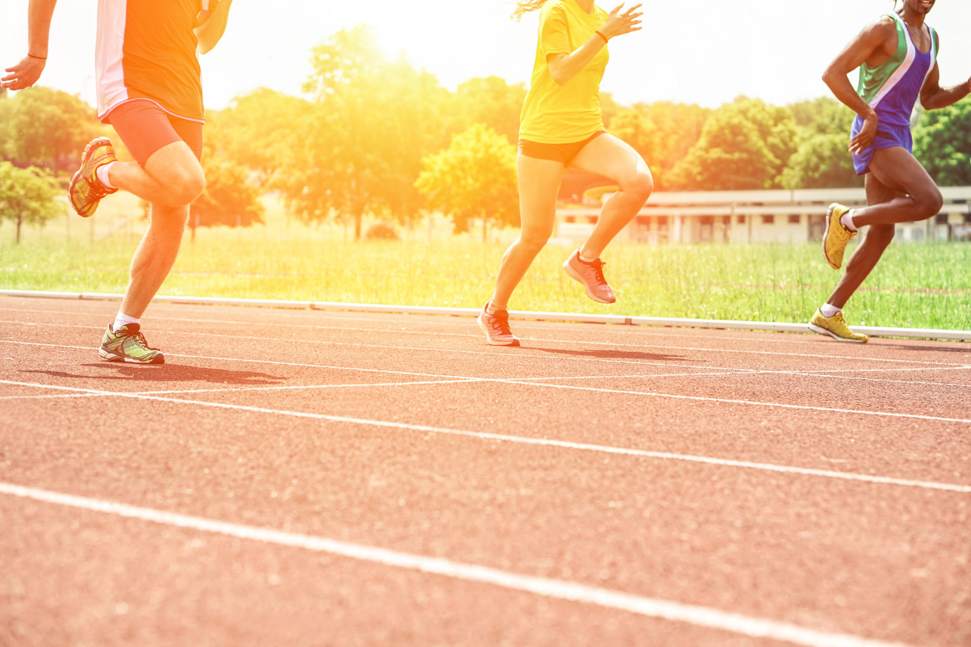 Athletes running on a synthetic athletics track at sunset